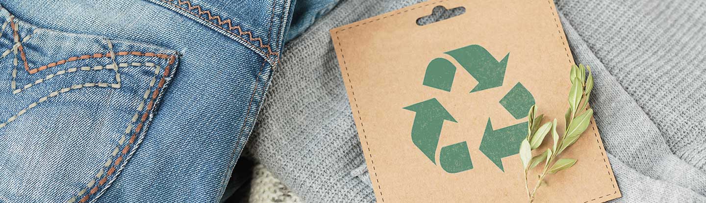 sullo sfondo jeans e maglione chiari, sopra una busta di cartone con simbolo riuso e riciclo