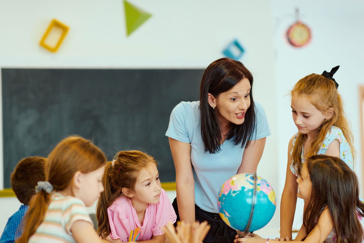 insegnante che spiega con il supporto di un mappamondo alle alunne della sua classe 